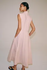 Vestido midi de Zara Woman Collection color rosado, confeccionado en hilatura de algodón. Presenta cuello subido con lazada, diseño sin mangas, bolsillos laterales ocultos y pliegues delanteros. Su falda tiene acabado en línea evasé y cuenta con cierre frontal mediante botones ocultos por solapa.