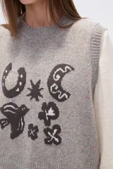 Chaleco de punto sin mangas en color beige con efecto confetti y diseño de jacquard frontal en color negro con motivos de herradura, luna y pájaro. Cuenta con cuello redondo y acabados acanalados.