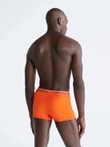 Pack de tres boxers tipo trunk de Calvin Klein, tiro bajo, confeccionados en microfibra elástica que absorbe la humedad. Incluye un boxer naranja, uno blanco/crema y uno beige/tostado, todos con cinturilla elástica con el logo de la marca.