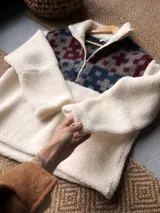 Buzo de corderito blanco con diseño de medio cierre frontal. Presenta un panel superior con estampado geométrico en tonos azul, gris y bordó, confeccionado con textiles vintage recuperados.