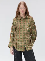 Camisa de seda con estampado geométrico de cuadrados en tonos verdes, ocres y rojos. Presenta cuello camisero, cierre frontal con botones, bolsillo en el pecho y mangas largas con puños abotonados.