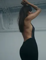 Vestido largo negro de corte ajustado, con espalda descubierta y detalle de tachas metálicas plateadas a lo largo de los laterales.