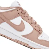 Championes Nike Dunk Low con diseño bicolor en blanco y rosa viejo. Presentan una silueta clásica de perfil bajo, con paneles de cuero, perforaciones en la puntera para mayor ventilación y suela de goma resistente.