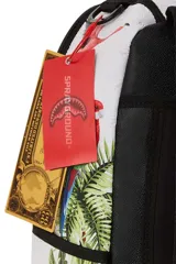 Mochila Sprayground con estampado de aves tropicales y vegetación selvática. Tiene un bolsillo con cremallera en la parte superior, dos bolsillos laterales con velcro, un bolsillo trasero con velcro, un bolsillo trasero con cremallera, correa para carro, espalda acolchada y transpirable, correas acolchadas y transpirables, cierre con cremallera de doble sentido, asa y accesorios de metal color oro pulido. El interior está forrado con poliéster con el logo de la marca, tiene un compartimento principal espacioso, dos bolsillos con cremallera, un compartimento acolchado para laptop.