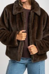 Abrigo de piel sintética en color marrón, con cuello clásico, cierre frontal con cremallera y mangas largas.