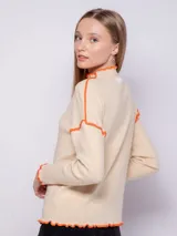 Polera de punto color beige con cuello alto, manga larga y detalles de costura overlock en color naranja.