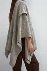 Capa de lana fina con cuello alto, cierre frontal con botones ocultos y bolsillos plaqué. Presenta aberturas laterales versátiles que permiten usarla como poncho o ruana, con terminaciones envivadas.