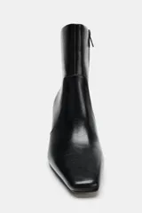 Botín de cuero sintético color negro, con diseño de punta cuadrada, cierre lateral mediante cremallera y tacón alto en bloque.