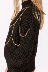 Sweater de punto grueso color negro, con cuello alto y diseño de cadenas doradas decorativas integradas en la parte frontal y hombros.