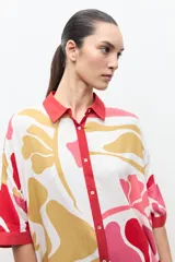 Túnica de corte recto y suelto con estampa floral en tonos de rosado, rojo y amarillo, cuello camisero rojo y mangas cortas holgadas.