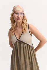 Vestido largo de silueta amplia y caída fluida, sin mangas, con escote en V y recorte bajo el busto. Combina un cuerpo superior beige con ribetes oscuros y una falda larga en color verde militar.