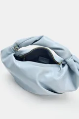 Bolso de mano celeste de diseño fruncido, con asa superior retorcida y cadena metálica dorada estilo bandolera. Cuenta con cierre de cremallera.