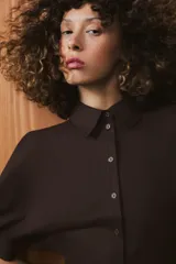 Vestido midi de algodón con cuello solapa, cierre frontal con botones y mangas cortas abullonadas con puños. Presenta un diseño evasé con bolsillos laterales ocultos y elástico en la espalda.