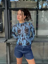 Top de manga larga, ajustado al cuerpo, confeccionado en microtul transparente con estampado floral en tonos marrones sobre fondo azul celeste. Presenta cuello redondo.