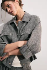 Chaqueta corta gris de tejido texturizado con cuello solapa, manga larga con trabilla, bolsillos delanteros con solapa y cierre frontal de botones metálicos.
