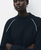 Sweater de punto color azul marino con cuello redondo y mangas largas. Presenta una línea vertical blanca contrastante que recorre el hombro y la parte superior de la manga.