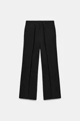 Pantalón de tiro medio color negro con trabillas en la cintura, bolsillos laterales ocultos y pierna recta. Cierre frontal con cremallera, botón y ganchos metálicos.