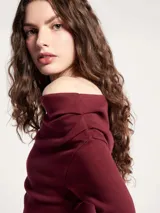 Blusa negra de manga larga con diseño asimétrico en el escote, dejando un hombro al descubierto. Presenta un corte ajustado con detalle de frunces laterales que crean un efecto drapeado en el torso.