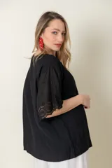 Blusa negra de viscosa con mangas cortas y detalle de broderie en los puños. Tiene cuello redondo y cierre frontal con botones.