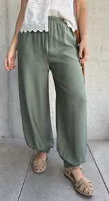 Pantalón tipo babucha de color verde militar, con cintura elástica fruncida y cordón ajustable. Cuenta con diseño amplio y puños elásticos en los tobillos.