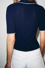 Top de punto confeccionado en mezcla de viscosa, color azul marino, de manga corta y cuello polo con solapas y escote en V. Presenta detalles de vivos a contraste en color blanco en el cuello, las mangas y el bajo.