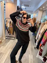 Sweater de punto tejido a mano en mohair, de color negro con diseño de guarda geométrica multicolor en tonos amarillo, naranja y rojo en la zona del canesú. Presenta cuello redondo y mangas largas con puños ajustados.