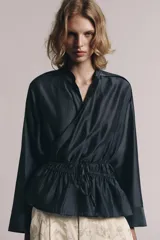 Blusa fluida cruzada de diseño envolvente, color gris oscuro satinado, con mangas largas y puños anchos. Cuenta con cuello mao y cordón ajustable en la cintura con lazada lateral.
