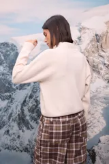 Buzo de tejido extra suave en color blanco, con cuello alto y cierre frontal parcial. Presenta mangas largas con puños ajustados y diseño de corte holgado.