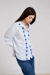 Camisa blanca de corte holgado con cuello camisero y cierre frontal de botones. Presenta un delicado bordado vertical de flores pequeñas en color bordó a lo largo de la botonera y en el cuello.