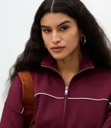 Campera de cuello alto en color bordó, con cierre frontal metálico y detalle de piping en contraste. Presenta puños y ruedo acanalados, con un diseño de corte deportivo y moderno.