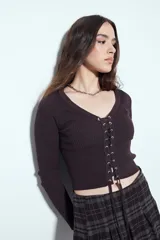 Top de tejido acanalado color negro, con escote en V y cierre frontal mediante cordones entrelazados con ojales metálicos. De manga larga y corte ajustado al cuerpo.