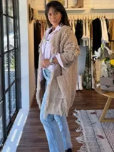 Sacón de punto color beige con flecos decorativos en los bordes y dos bolsillos delanteros.