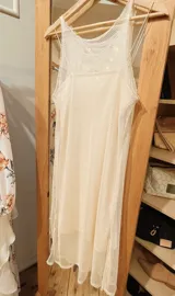 Vestido de red color crudo, con escote alto y largo midi. Incluye un forro interior independiente más corto, con escote recto y breteles finos.