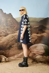 Vestido corto de punto jacquard color azul marino, con diseño de estrellas blancas alineadas verticalmente en los laterales. Presenta cuello polo con cierre frontal de botones y mangas cortas con detalles de rayas en contraste.