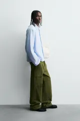 Camisa de algodón de corte regular, color celeste con finas rayas blancas verticales. Presenta un bordado en color rojo en el pecho con la frase "Café du Matin Doux".