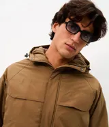 Campera utilitaria de poliéster color tostado, con capucha ajustable, cuello alto, cierre frontal con cremallera y solapa con botones a presión, y bolsillos frontales grandes con solapa.