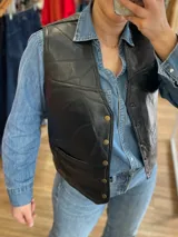 Chaleco negro de cuero con diseño de paneles geométricos y botones dorados.