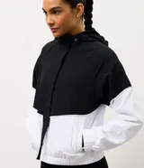 Campera rompeviento deportiva con diseño bicolor en negro y blanco. Presenta capucha con cordón ajustable, cierre frontal y puños elásticos.