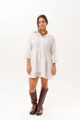 Vestido corto de broderie color crudo, con cuello camisero, cierre frontal parcial con botones, mangas tres cuartos acampanadas y corte evasé con volados.