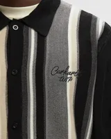 Cárdigan de punto con cuello polo, manga larga negra y cuerpo a rayas verticales en tonos negro, gris y beige. Presenta un pequeño bordado en el pecho.