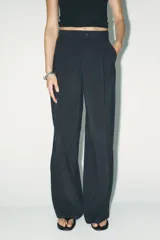 Pantalón de tiro alto color rojo vibrante, de corte ancho y pierna recta, con pliegues marcados en la parte delantera. Presenta cierre frontal con botón y cremallera, y bolsillos delanteros.