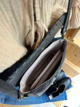 Cartera bandolera de cuero negro con textura tipo cocodrilo, correa larga regulable y forro interno de tela.