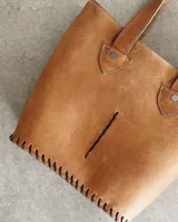 Bolso tipo tote de cuero color marrón claro, con doble asa de hombro, detalle de costuras a la vista y abertura frontal.