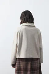 Campera corta de paño color gris con cuello de corderito blanco, cierre frontal con botones y bolsillos laterales.