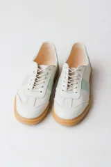 Zapatilla de cuero color crudo con detalle de una franja lateral en verde agua y cordones color beige.