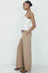 Pantalón de tiro alto color marrón, de corte recto y holgado, con bajo acabado en vuelta. Incluye bolsillos delanteros y cinturón fino a contraste con hebilla metálica.
