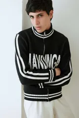 Campera tejida de algodón en color negro con detalles en blanco, cuello alto con cierre frontal completo, franjas blancas en las mangas y la palabra Mandinga estampada en el pecho.