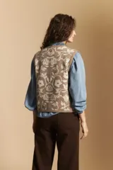 Chaleco tejido de corte recto y sin mangas, con diseño floral ornamental en tonos beige y marrón. Presenta cierre frontal con botones y cuello redondo.