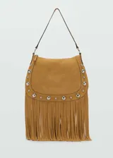 Bolso de hombro color tostado, confeccionado en piel bovina con acabado de gamuza. Presenta un diseño decorado con tachuelas metálicas plateadas en los bordes y flecos largos en la parte inferior. Incluye cierre de cremallera y forro interior de algodón.