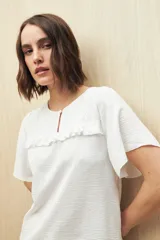 Blusa blanca con textura sutil, detalle de encaje en el canesú y volados. Tiene corte fluido y mangas cortas amplias.